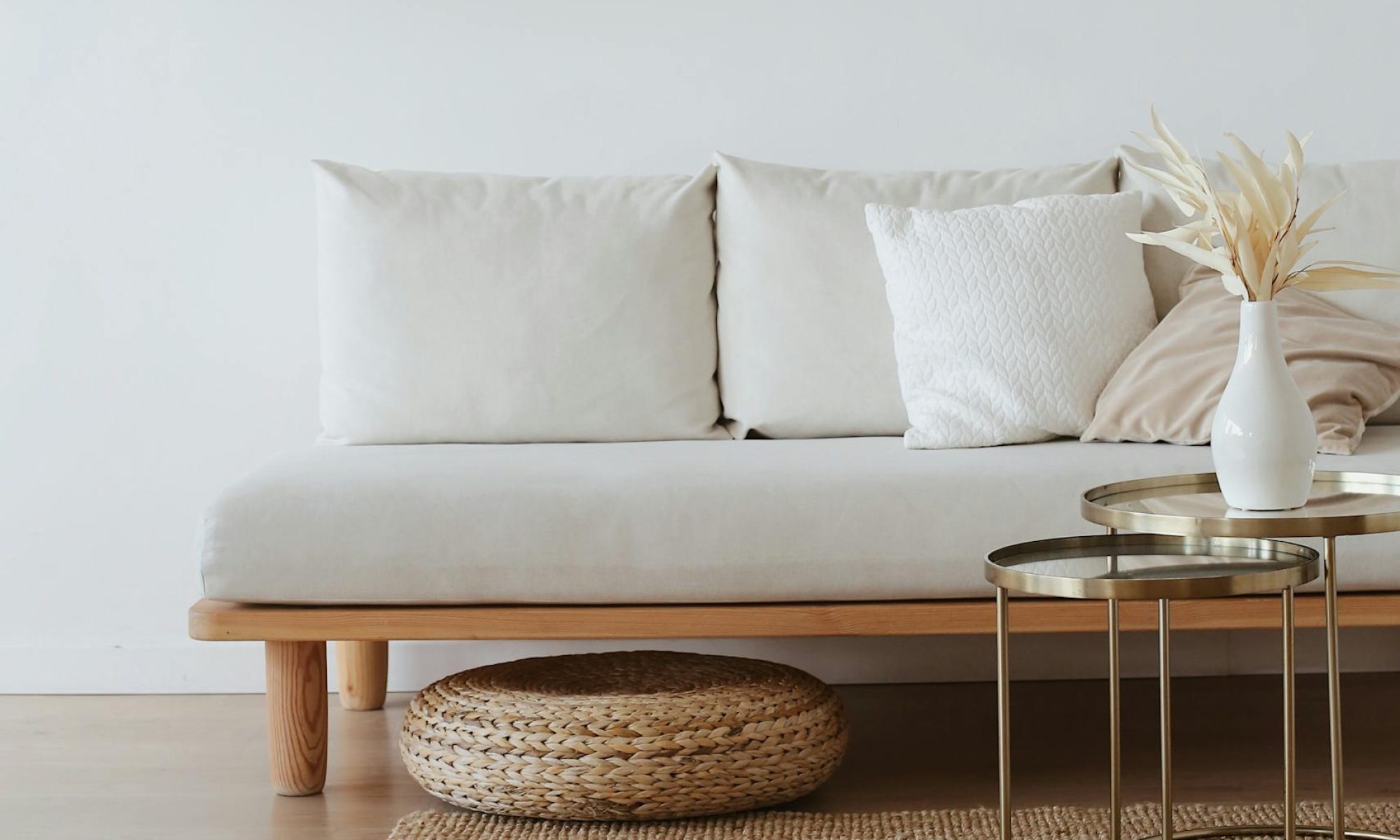 Contemporary living. Cream sofa cushions on low wooden frame. seagrass matting, contemporary nest of round glass coffee tables with simple white vase and dried grasses in neutral tones . cushions on sofa are in soft off white tones. The image is suggestive of a contemporary, no-fuss, effective, tasteful and expensive business.