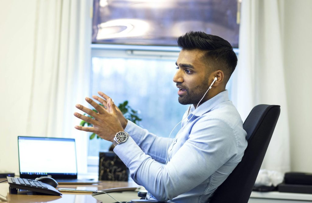 Adult Asian male engaged in a virtual meeting using earphones in an office setting. This image is used to suggest the demographic of Therapeutic Consultancy 
